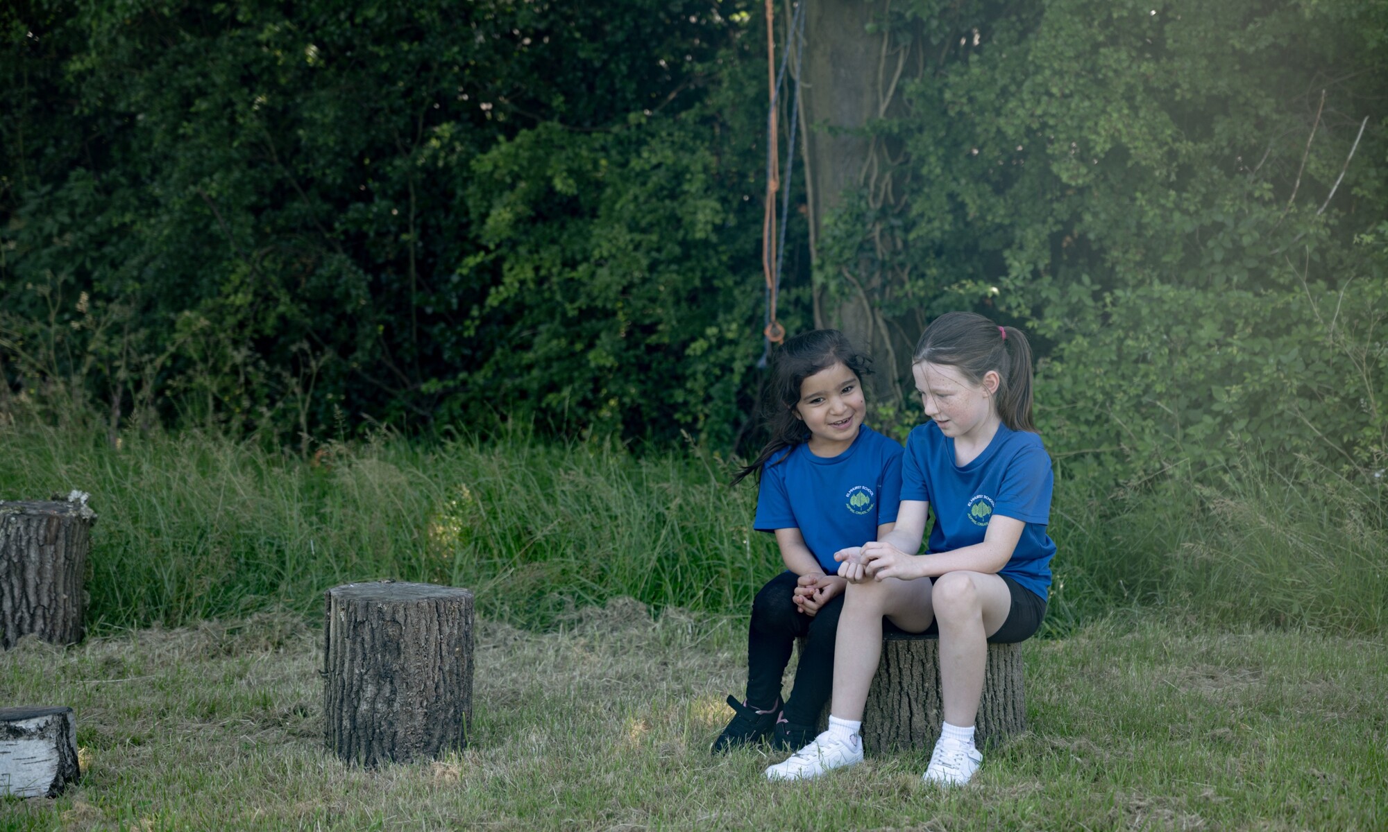 Elmhurst school two girls sitting on logs in the school garden